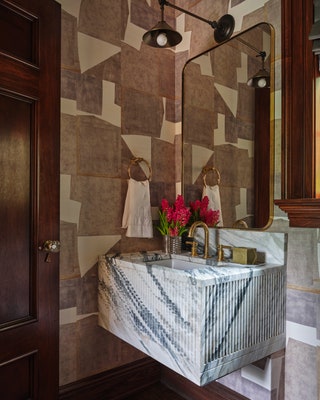 Odom designed a custom Orobico marble vanity for a powder room wrapped in a Christopher Farr raffia wallcovering. An...